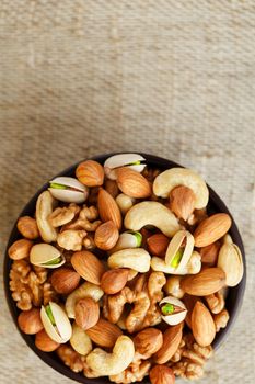 Mix of nuts of cashew, almonds, pistachios, hazelnuts and walnuts is against the background of brown fabric of burlap. Nuts as structure and background, macro