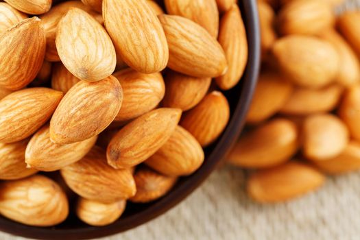 Almonds in a wooden cup on a burlap cloth background. Golden almond closeup in dark brown cup