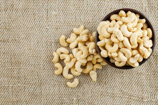 Cashew nuts in a wooden bowl on a burlap cloth background. Golden cashew close-up in a dark brown cup.