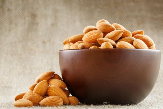 Almonds in a wooden cup on a burlap cloth background. Golden almond closeup in dark brown cup