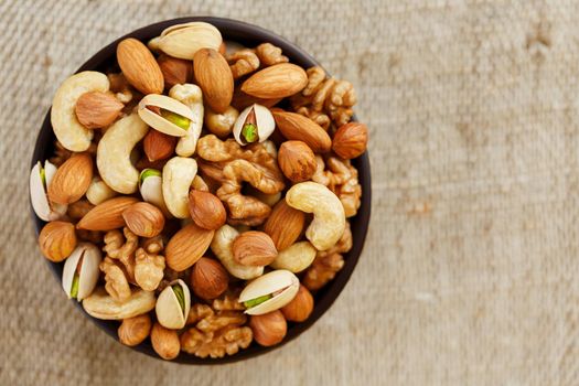 Mix of nuts of cashew, almonds, pistachios, hazelnuts and walnuts is against the background of brown fabric of burlap. Nuts as structure and background, macro