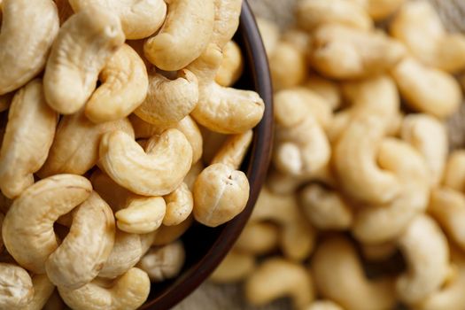 Cashew nuts in a wooden bowl on a burlap cloth background. Golden cashew close-up in a dark brown cup.