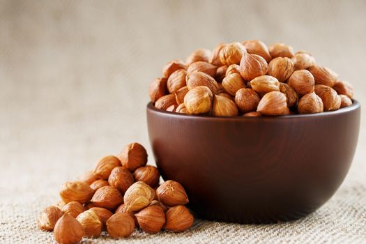 Peeled hazelnuts in a wooden, dark brown cup on a burlap cloth. Super Food, Raw. View from above.