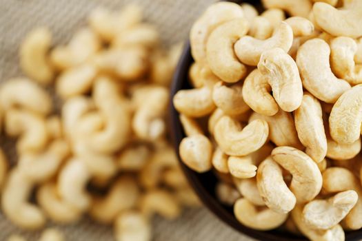 Cashew nuts in a wooden bowl on a burlap cloth background. Golden cashew close-up in a dark brown cup.