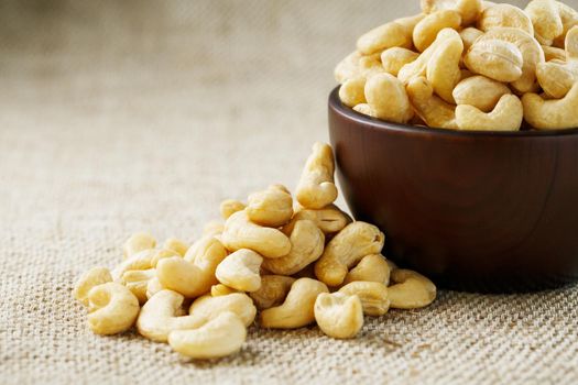 Cashew nuts in a wooden bowl on a burlap cloth background. Golden cashew close-up in a dark brown cup.