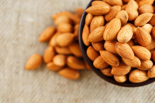 Almonds in a wooden cup on a burlap cloth background. Golden almond closeup in dark brown cup