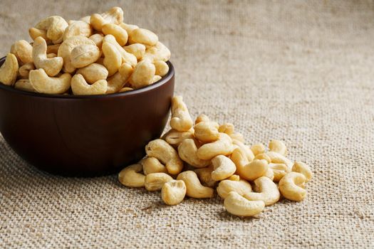 Cashew nuts in a wooden bowl on a burlap cloth background. Golden cashew close-up in a dark brown cup.