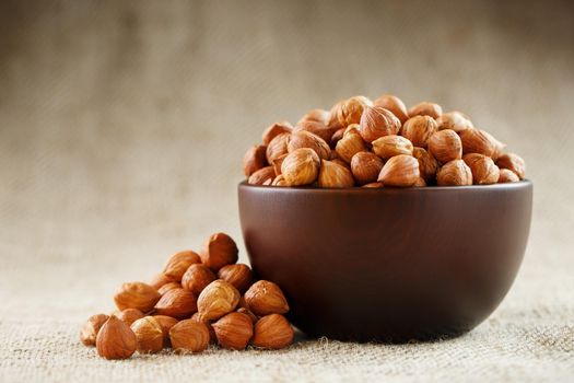 Peeled hazelnuts in a wooden, dark brown cup on a burlap cloth. Super Food, Raw. View from above.