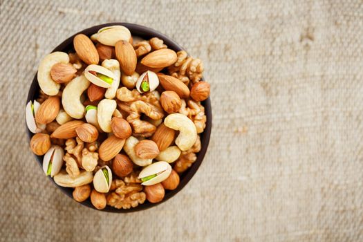 Mix of nuts of cashew, almonds, pistachios, hazelnuts and walnuts is against the background of brown fabric of burlap. Nuts as structure and background, macro