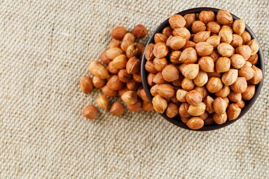 Peeled hazelnuts in a wooden, dark brown cup on a burlap cloth. Super Food, Raw. View from above.