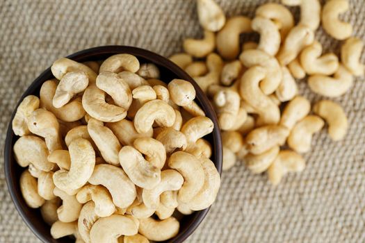 Cashew nuts in a wooden bowl on a burlap cloth background. Golden cashew close-up in a dark brown cup.