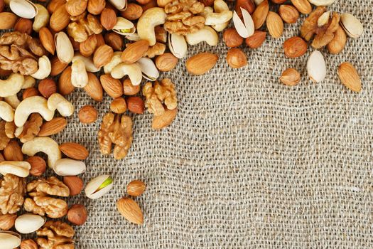 Mix of nuts of cashew, almonds, pistachios, hazelnuts and walnuts is against the background of brown fabric of burlap. Nuts as structure and background, macro