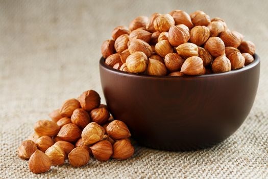 Peeled hazelnuts in a wooden, dark brown cup on a burlap cloth. Super Food, Raw. View from above.