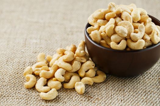 Cashew nuts in a wooden bowl on a burlap cloth background. Golden cashew close-up in a dark brown cup.
