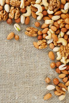 Mix of nuts of cashew, almonds, pistachios, hazelnuts and walnuts is against the background of brown fabric of burlap. Nuts as structure and background, macro