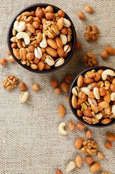 A mixture of cashew nuts, almond nuts, pistachios, hazelnuts and walnuts in a wooden cup against the background of burlap fabric. Nuts as structure and background, macro. Two cups of nuts.