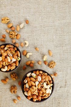 A mixture of cashew nuts, almond nuts, pistachios, hazelnuts and walnuts in a wooden cup against the background of burlap fabric. Nuts as structure and background, macro. Two cups of nuts.