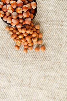 Peeled hazelnuts in a wooden, dark brown cup on a burlap cloth. Super Food, Raw. View from above.