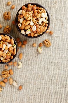 A mixture of cashew nuts, almond nuts, pistachios, hazelnuts and walnuts in a wooden cup against the background of burlap fabric. Nuts as structure and background, macro. Two cups of nuts.