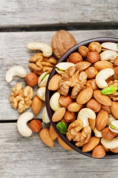 Wooden bowl with mixed nuts on a wooden gray background. Healthy food and snacks, organic vegetarian meals. Walnut, pistachios, almonds, hazelnuts and cashews, walnut.