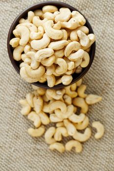 Cashew nuts in a wooden bowl on a burlap cloth background. Golden cashew close-up in a dark brown cup.