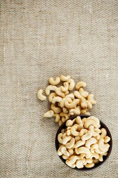 Cashew nuts in a wooden bowl on a burlap cloth background. Golden cashew close-up in a dark brown cup.