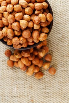 Peeled hazelnuts in a wooden, dark brown cup on a burlap cloth. Super Food, Raw. View from above.