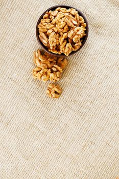 Peeled walnuts in a wooden, dark brown cup on a burlap cloth. Super Food, Raw. View from above.