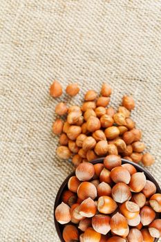 Peeled hazelnuts in a wooden, dark brown cup on a burlap cloth. Super Food, Raw. View from above.