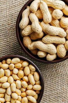 Peanuts in the shell and peeled close up in a cup. Background with peanuts. Roasted peanuts in the shell and peeled on a background of brown cloth in cups