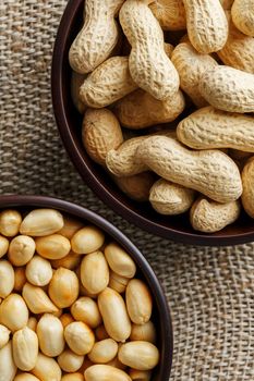 Peanuts in the shell and peeled close up in a cup. Background with peanuts. Roasted peanuts in the shell and peeled on a background of brown cloth in cups