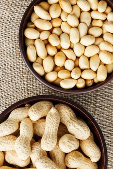 Peanuts in the shell and peeled close up in a cup. Background with peanuts. Roasted peanuts in the shell and peeled on a background of brown cloth in cups