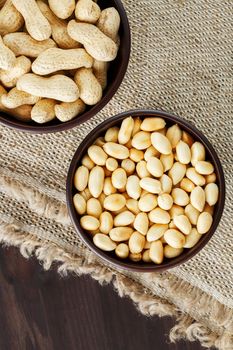 Peanuts in the shell and peeled closeup in a cup. Background with peanuts. Roasted peanuts in the shell and peeled on a background of brown cloth in cups