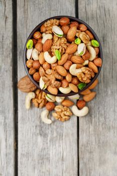 Wooden bowl with mixed nuts on a wooden gray background. Healthy food and snacks, organic vegetarian meals. Walnut, pistachios, almonds, hazelnuts and cashews, walnut.