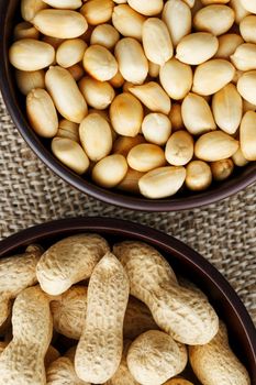 Peanuts in the shell and peeled close up in a cup. Background with peanuts. Roasted peanuts in the shell and peeled on a background of brown cloth in cups