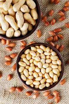 Peanuts in the shell and peeled closeup in a cup. Background with peanuts. Roasted peanuts in the shell and peeled on a background of brown cloth in cups