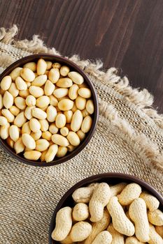 Peanuts in the shell and peeled closeup in a cup. Background with peanuts. Roasted peanuts in the shell and peeled on a background of brown cloth in cups