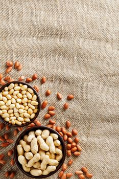 Peanuts in the shell and peeled closeup in a cup. Background with peanuts. Roasted peanuts in the shell and peeled on a background of brown cloth in cups