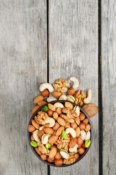 Wooden bowl with mixed nuts on a wooden gray background. Healthy food and snacks, organic vegetarian meals. Walnut, pistachios, almonds, hazelnuts and cashews, walnut.