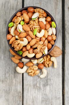 Wooden bowl with mixed nuts on a wooden gray background. Healthy food and snacks, organic vegetarian meals. Walnut, pistachios, almonds, hazelnuts and cashews, walnut.