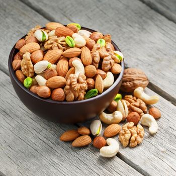 Wooden bowl with mixed nuts on a wooden gray background. Healthy food and snacks, organic vegetarian meals. Walnut, pistachios, almonds, hazelnuts and cashews, walnut.