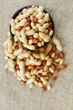 Peanuts in the shell and peeled close up in a cup. Background with peanuts. Roasted peanuts in the shell and peeled on a background of brown cloth in cups