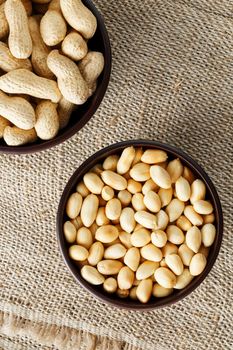 Peanuts in the shell and peeled close up in a cup. Background with peanuts. Roasted peanuts in the shell and peeled on a background of brown cloth in cups