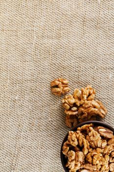 Peeled walnuts in a wooden, dark brown cup on a burlap cloth. Super Food, Raw. View from above.