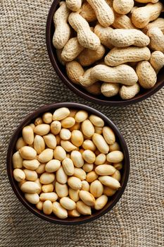 Peanuts in the shell and peeled closeup in a cup. Background with peanuts. Roasted peanuts in the shell and peeled on a background of brown cloth in cups