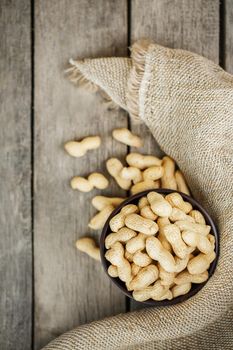 Peanuts in shell, in a wooden brown cup on a gray wooden table. Organic vegetarian protein, macro.