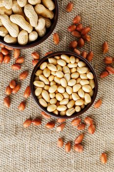 Peanuts in the shell and peeled closeup in a cup. Background with peanuts. Roasted peanuts in the shell and peeled on a background of brown cloth in cups