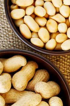 Peanuts in the shell and peeled close up in a cup. Background with peanuts. Roasted peanuts in the shell and peeled on a background of brown cloth in cups