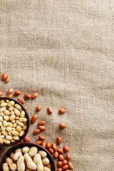 Peanuts in the shell and peeled closeup in a cup. Background with peanuts. Roasted peanuts in the shell and peeled on a background of brown cloth in cups