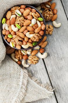 Wooden bowl with nuts on a wooden background, near a bag from burlap. Healthy food and snack, organic vegetarian food. Walnut, pistachios, almonds, hazelnuts and nuts of cashew, walnut. Top view.